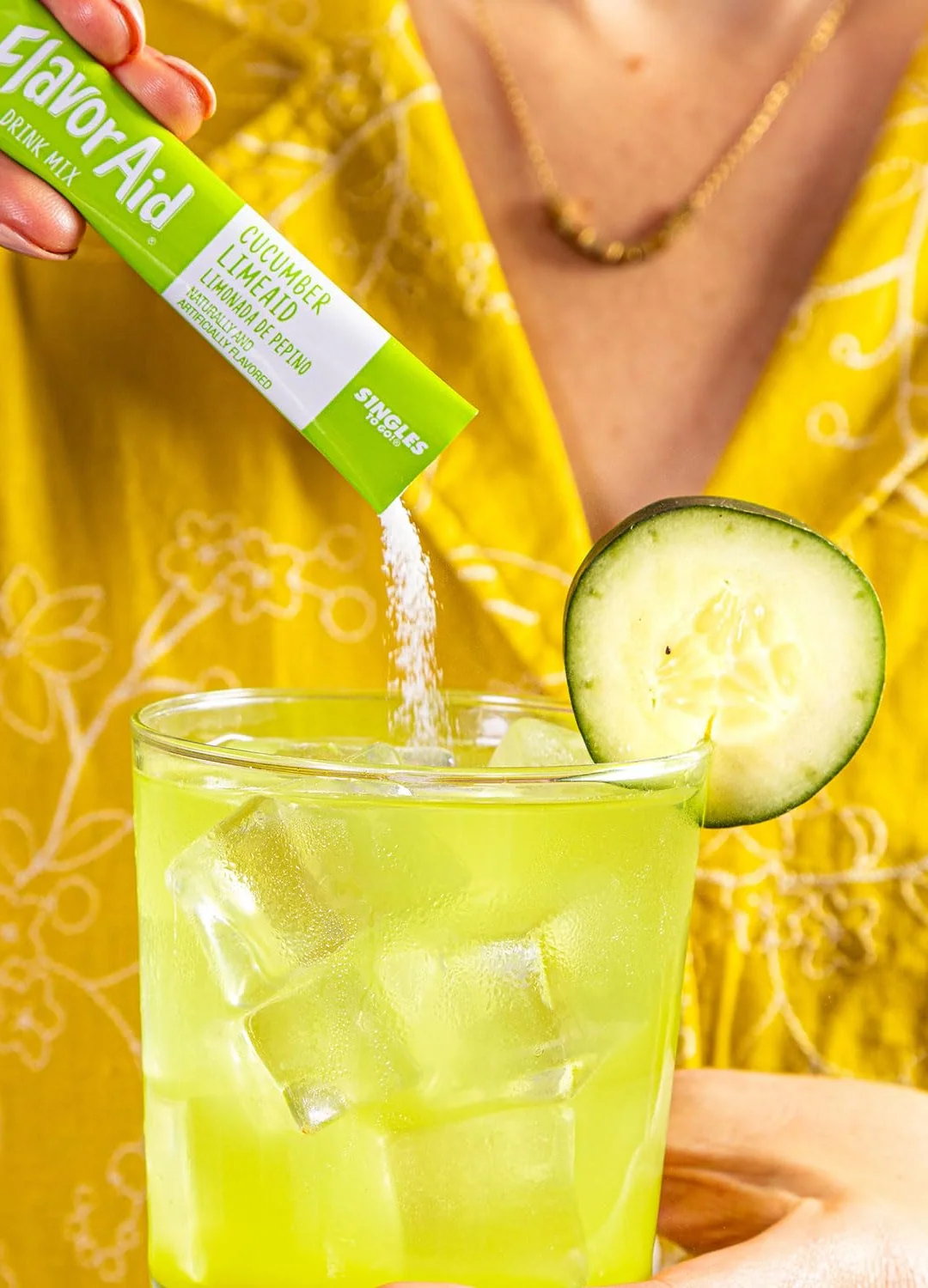 A Flavor Aid Cucumber Limeaid stick poured into a glass of ice water with a cucumber slice